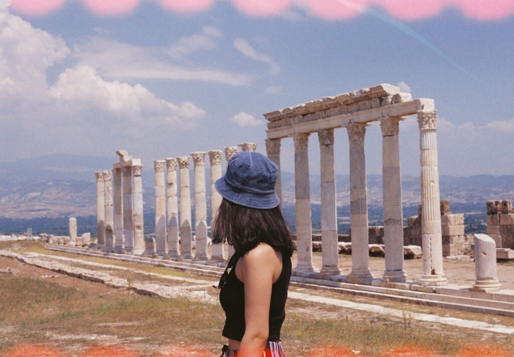 A woman observes the majestic columns of ancient Greek ruins under a clear blue sky.